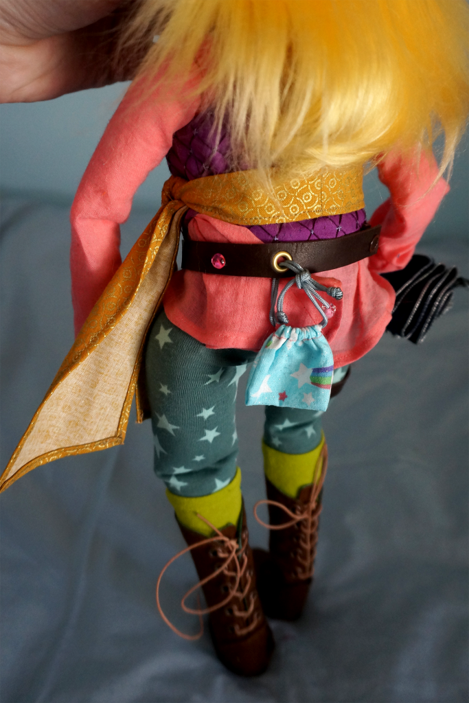 Taako's outfit has no real color scheme, with a pink shirt, purple vest, gold tied belt, green-blue star pants and lime green socks